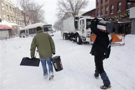 Men with a shovel and buckets of salt pass a snow plow and city bus that were both stuck on Monday in Brooklyn, N.Y.